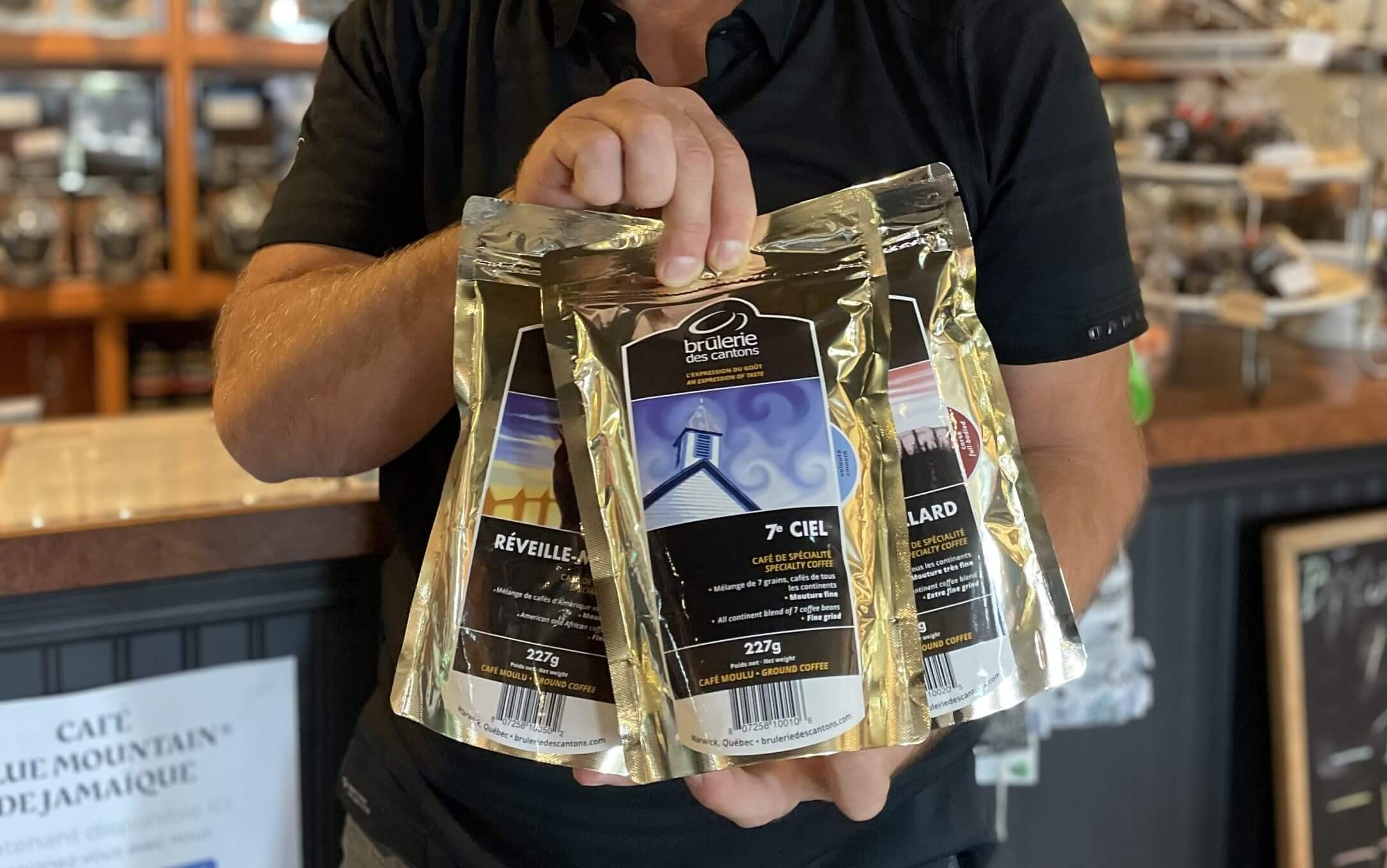 Deux mains tenant des sacs de café de spécialité torréfié à la Brûlerie des Cantons.