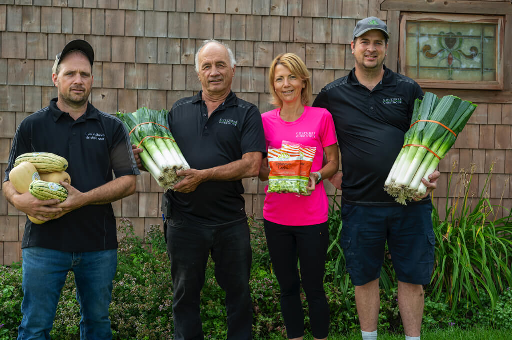 Quatre membres de la famille derrière Les cultures de chez nous tenant fièrement leurs légumes récoltés à la ferme.
