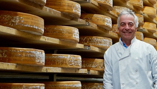 Un fromager de la Fromagerie du Presbytère devant un étalage de meules de fromage.
