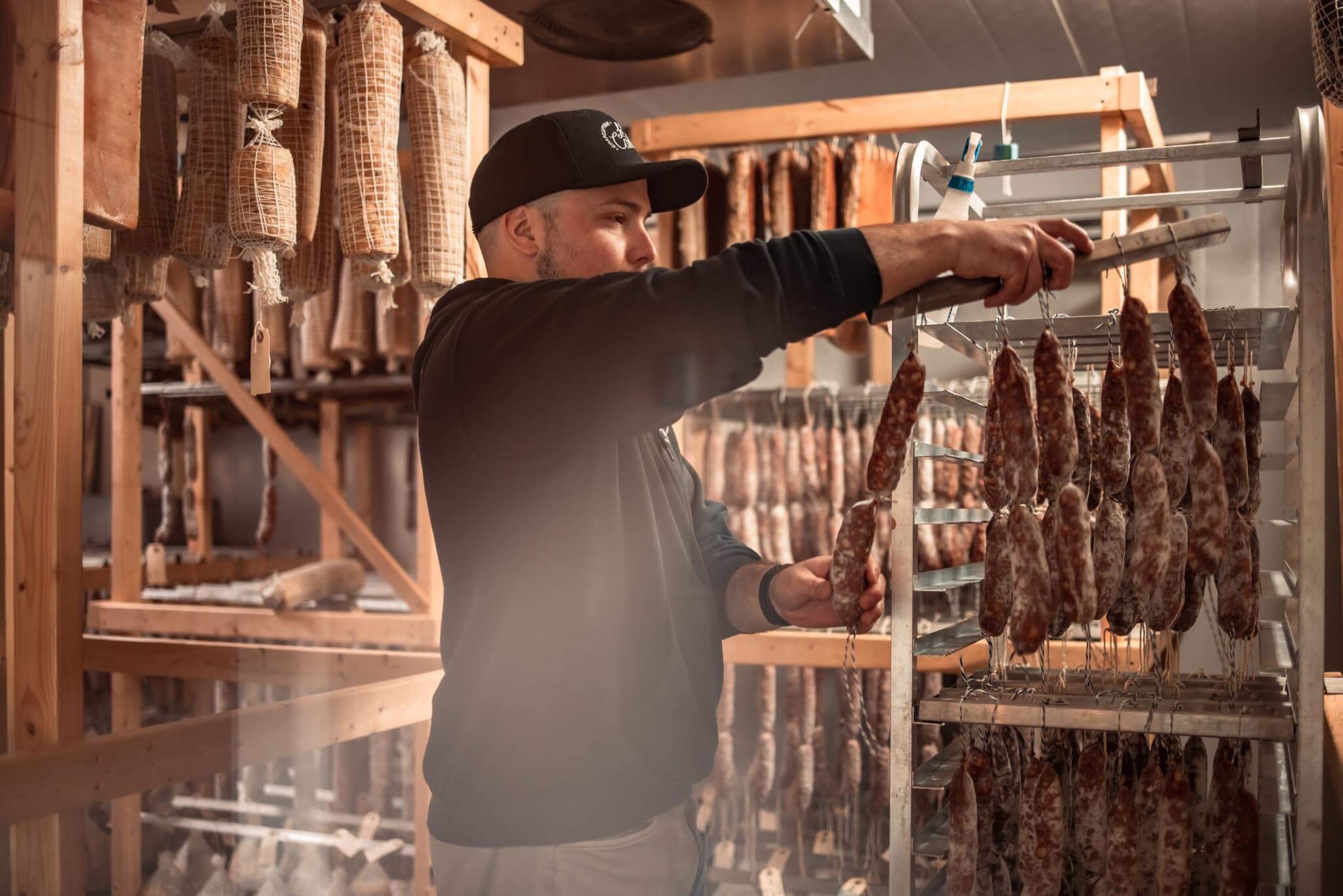 Le propriétaire de La Cantina manipulant des saucissons dans la salle de séchage.