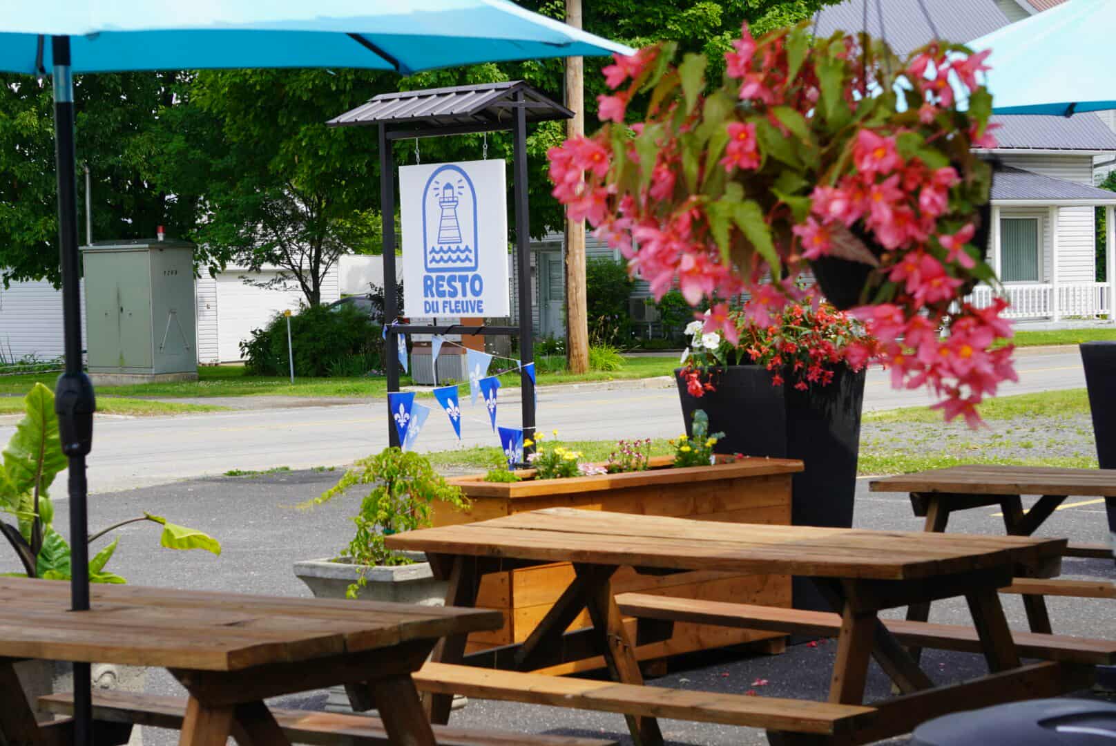 Terrasse du Resto du Fleuve, aménagée avec des tables à pique-nique en bois et des bacs à fleurs colorés.