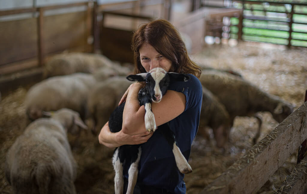 La propriétaire de la ferme Aux 13 Arpents dans l'étable avec un agneau dans ses bras.